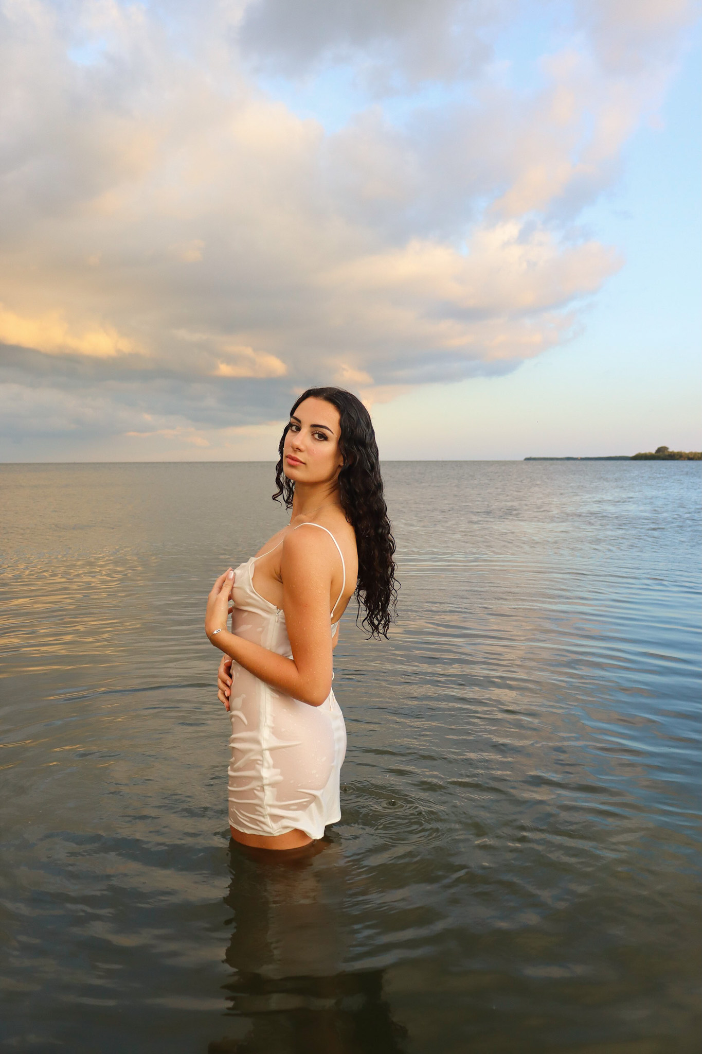 Sunset Beach Portrait Photography in St Petersburg Woman in white dress standing in ocean water during golden hour in St Petersburg Florida