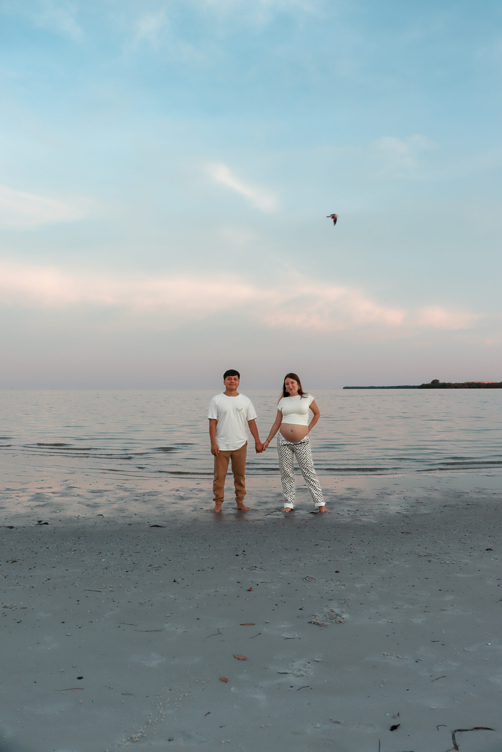 Couple holding hands on the beach at sunset maternity shoot in Tampa