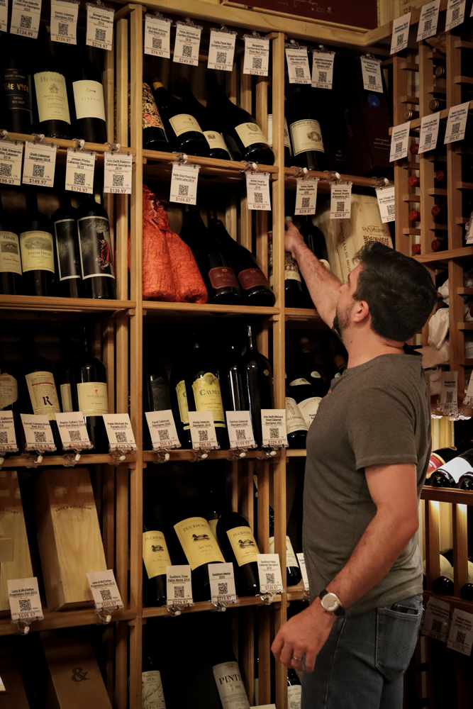 Wine Inventory Moment – Redneck Wine Staff member reading label from a wooden wine shelf