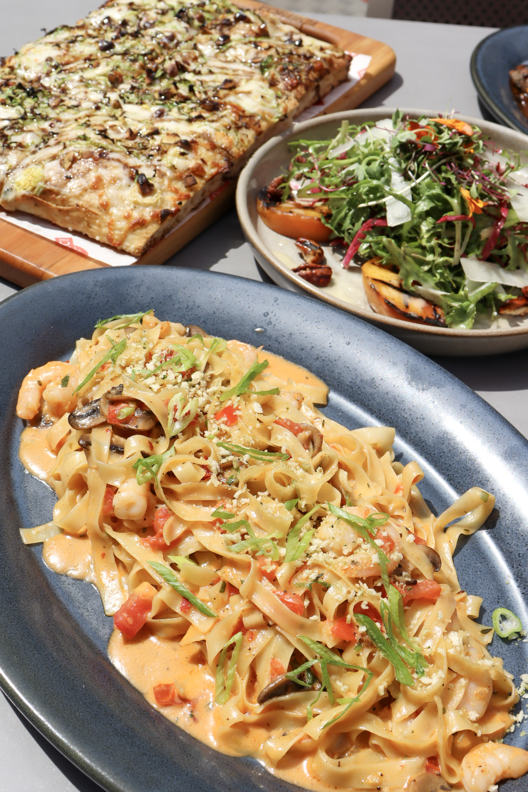 Pasta, Flatbread, and Salad Photography – Tampa Food Branding Creamy pasta dish with vegetables, flatbread pizza, and colorful salad on outdoor restaurant table